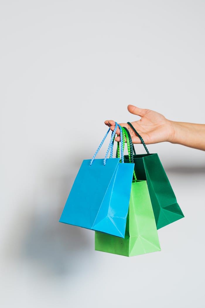 Hand holding three colorful paper shopping bags on a white background.